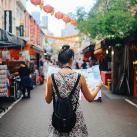 Rear view image of a young brunette woman. She is enjoying the walk and exploring the city, wearing a casual but fashionable dress, sightseeing and shopping on the Singapore street market. She is holding a large city map, checking out where to go next.