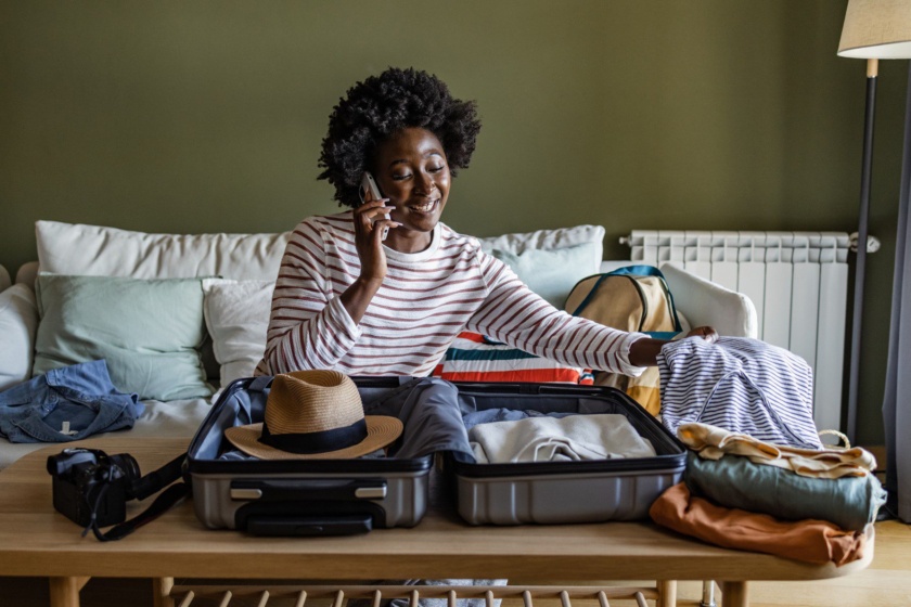 Young woman preparing for a trip. She is sitting on the couch and using smart phone